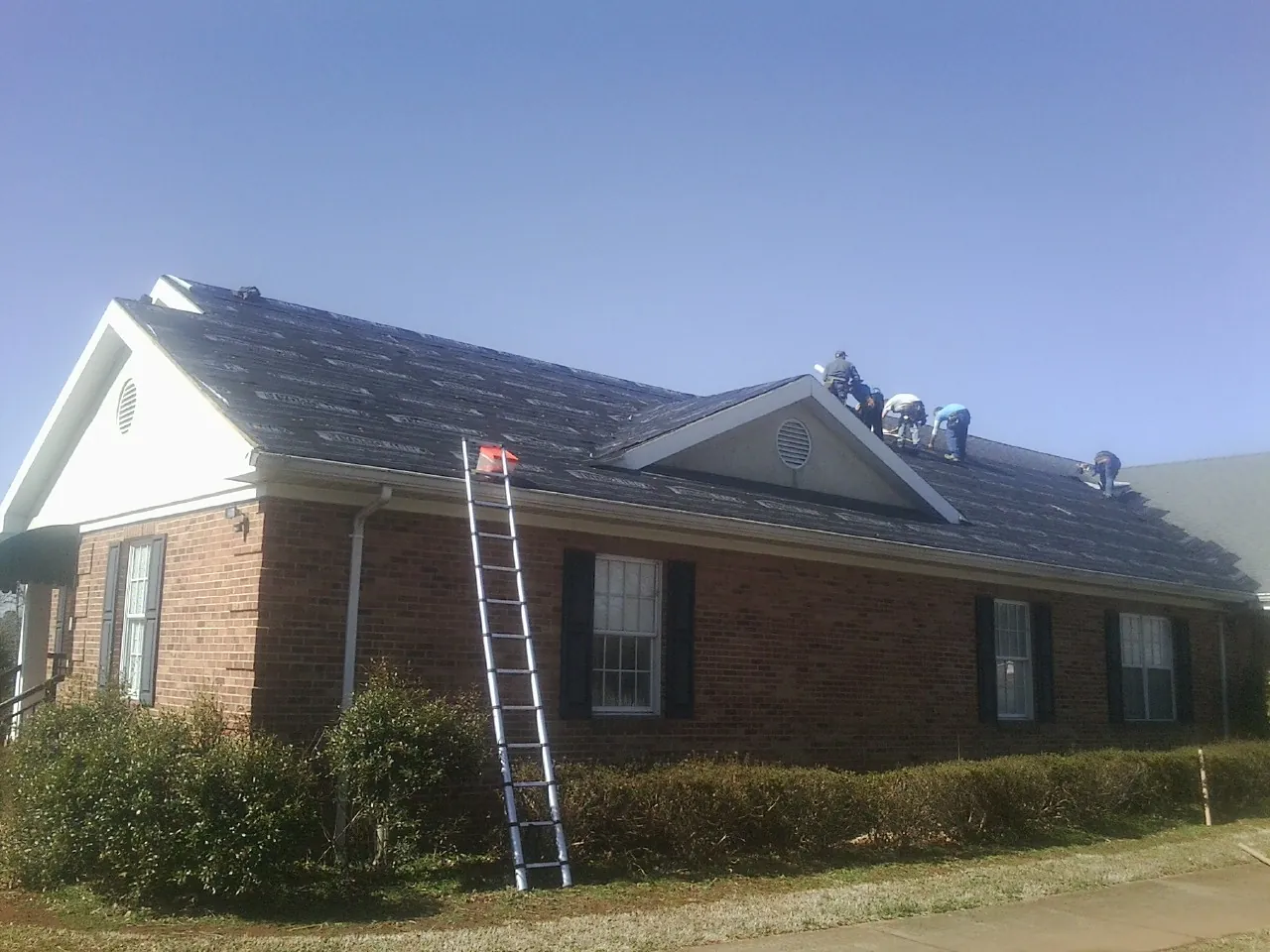 Crew tearing shingles off a brick ranch roof with a ladder set — Emergency Roof Repair work by our crew in Waterman