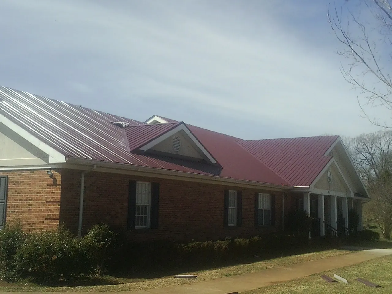 Red metal roof with gabled entries on a long brick building, from a Hail Damage Roof Repair job in Waterman