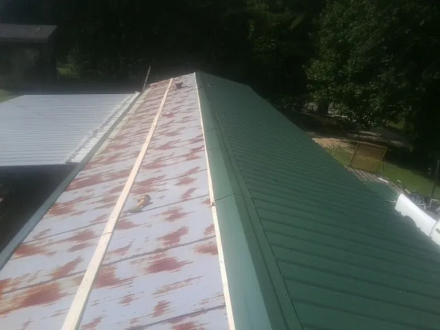 Old rusted panels beside newly installed green metal roofing — Wind Damage Roof Repair by Roofing Brothers in Waterman