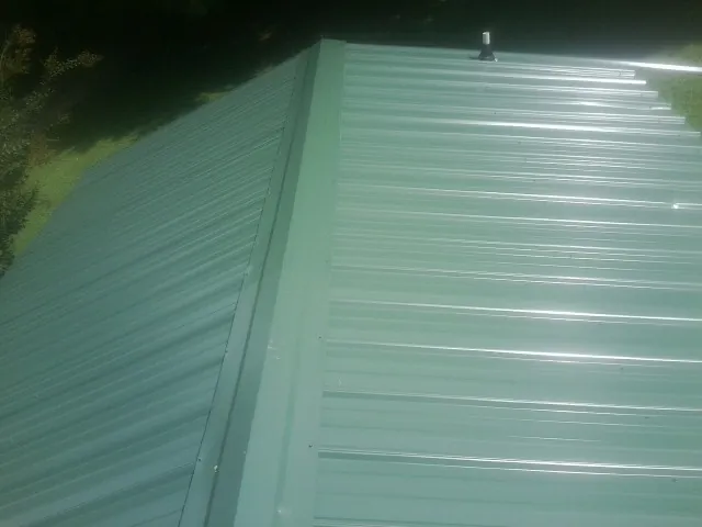 New green metal panels meeting at the ridge of a roof — Flat Roof Repair work by our crew in Waterman
