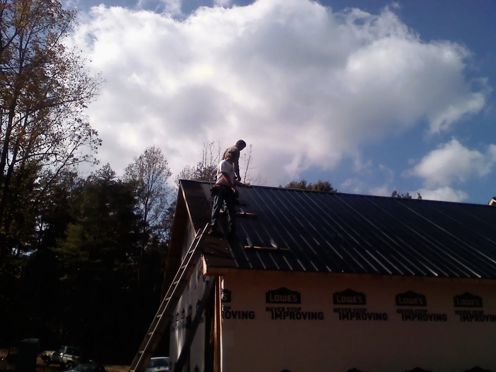 Roofer fastening dark metal panels high against a cloudy sky, from a Roof Inspection job in Waterman