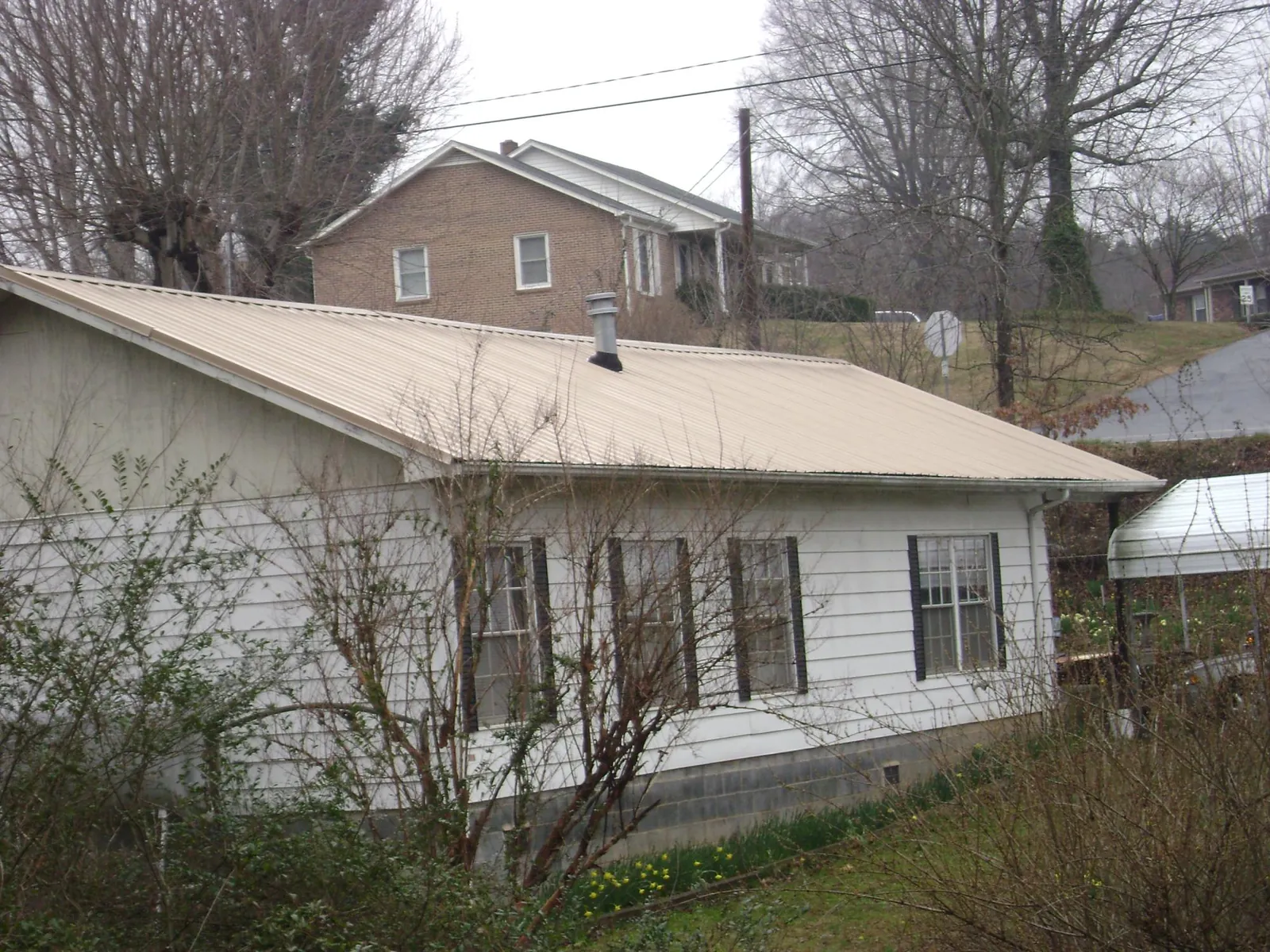 Tan metal roof on a white sided house set into a hillside — Commercial Roofing by Roofing Brothers in Waterman