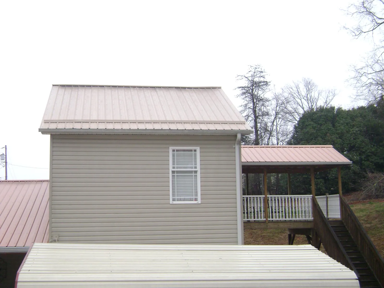 Tan metal roofs on a two story addition and attached porch, from a Roof Replacement job in Waterman